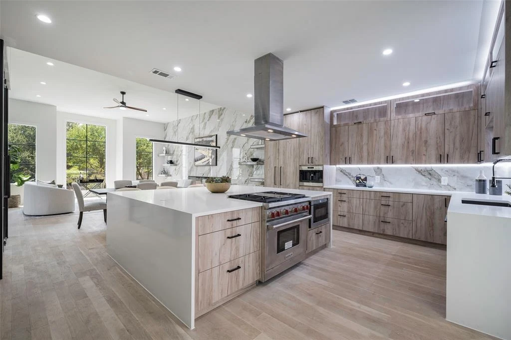 Elysian kitchen looking toward the living room, with a Wolf range, warm wood cabinetry, and a marble fireplace wall
