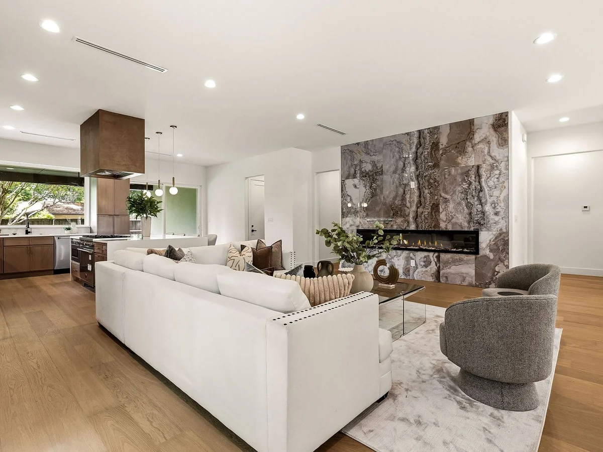 The Westchester kitchen opening into the living room, with warm wood cabinetry and a marble fireplace wall
